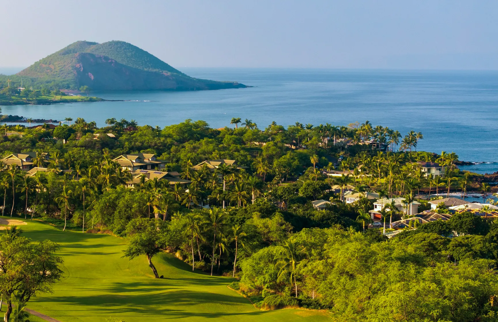 Coastal fairway and palm-lined villas looking out over a bay and a volcanic headland