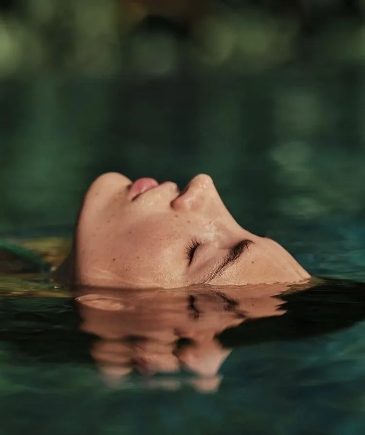 Woman floating on her back in dark green water, eyes closed
