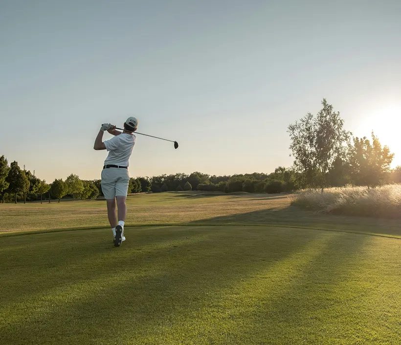 Golfer mid-swing on a fairway at sunset