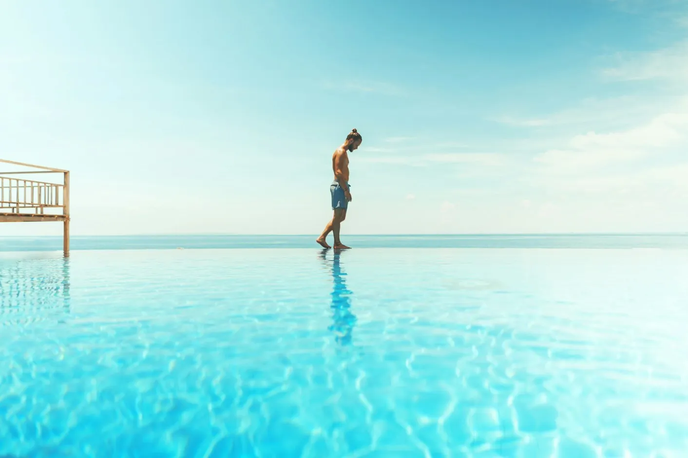Person walking along the edge of an infinity pool meeting the sea