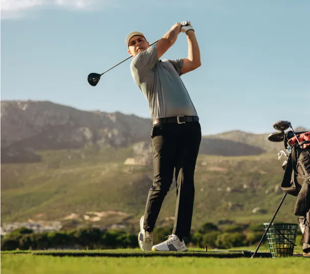 Golfer driving off a tee with mountains behind