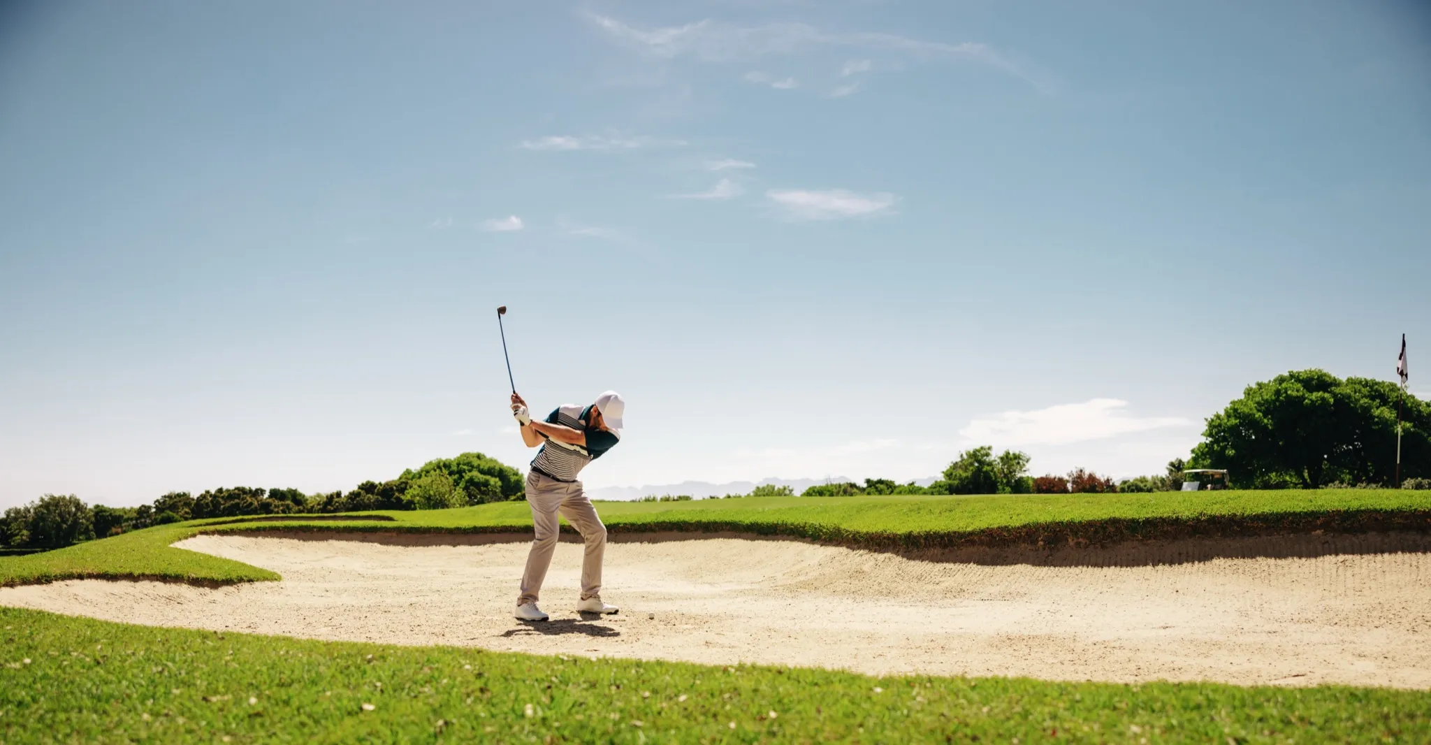Golfer playing out of a greenside bunker under a clear blue sky