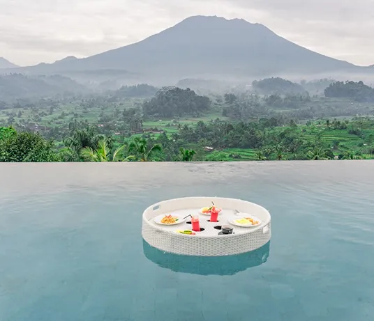 Infinity pool with a floating breakfast tray facing a volcano